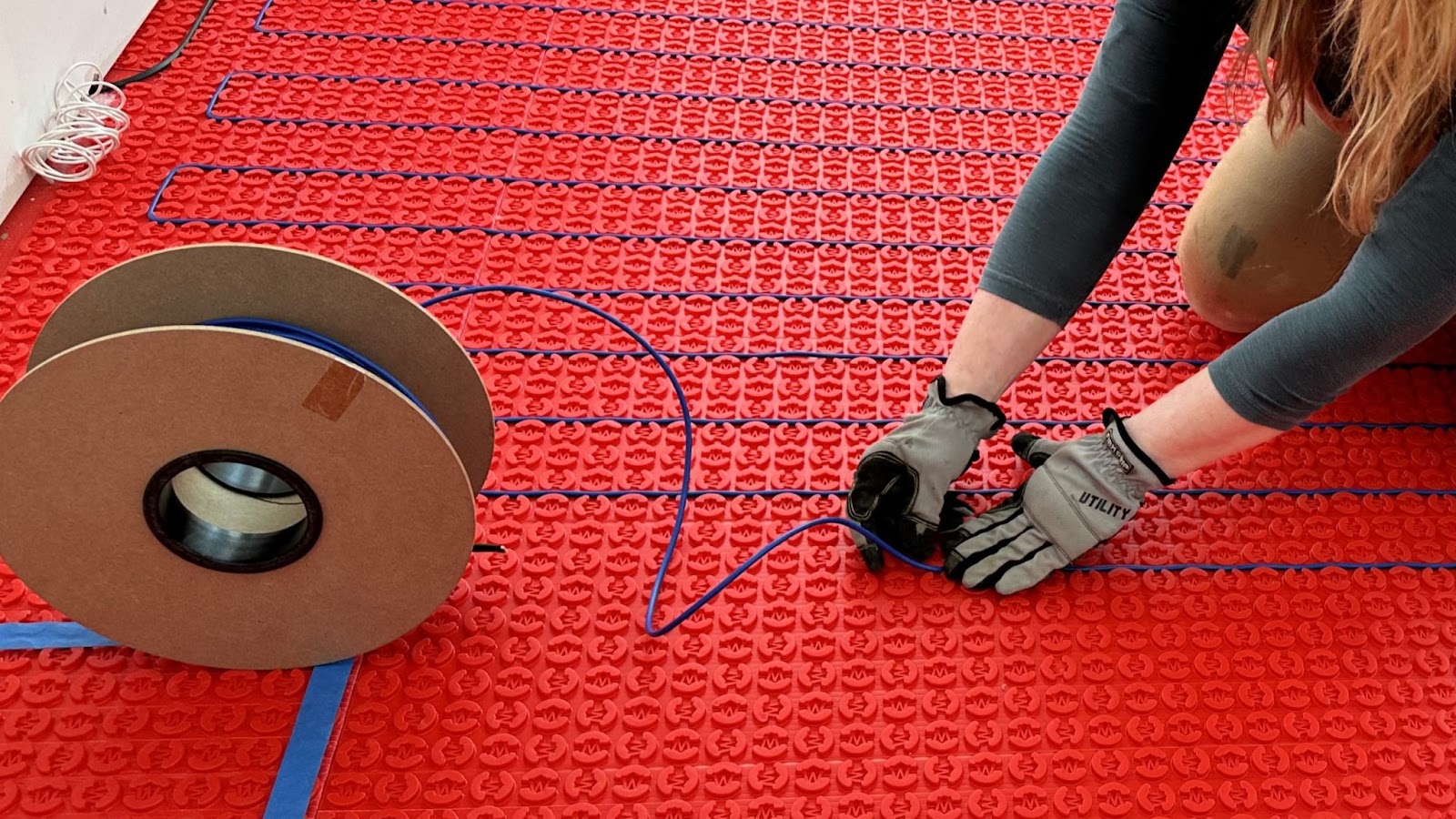 Ultimate Guide to Radiant Floor Heating- A worker installs the heating system into the floor of a house.